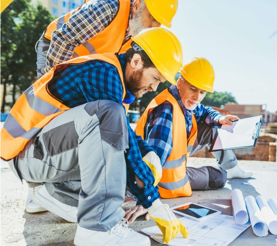 handsome-construction-workers-sitting-on-concrete-at-construction-site-discussing-building-plans-1.jpg